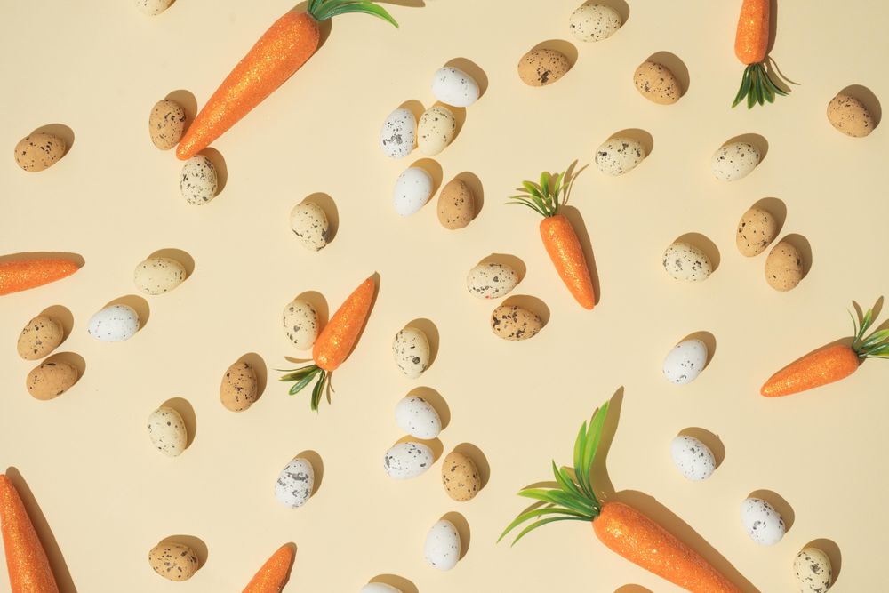 Easter eggs and carrots on pastel yellow background