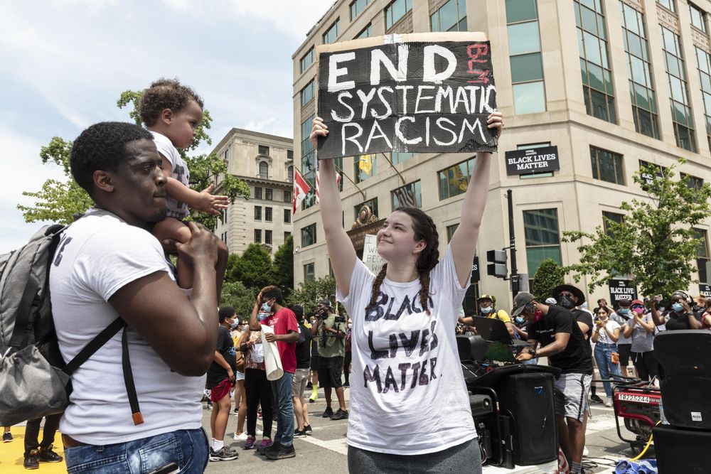 Woman holding anti-racism sign next to father with son on shoulders, Washington, D.C.