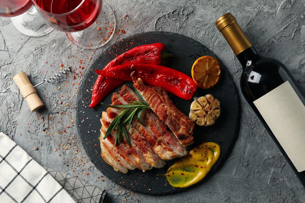 Chopped fried pork steak, vegetables and wine on gray background. Grilled food