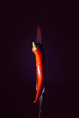 red chili pepper on fire in fork on a dark background