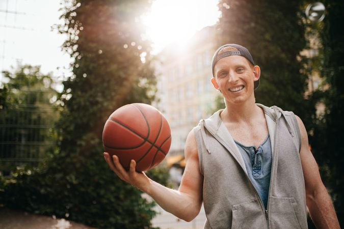Smiling young man holding a basketball on court