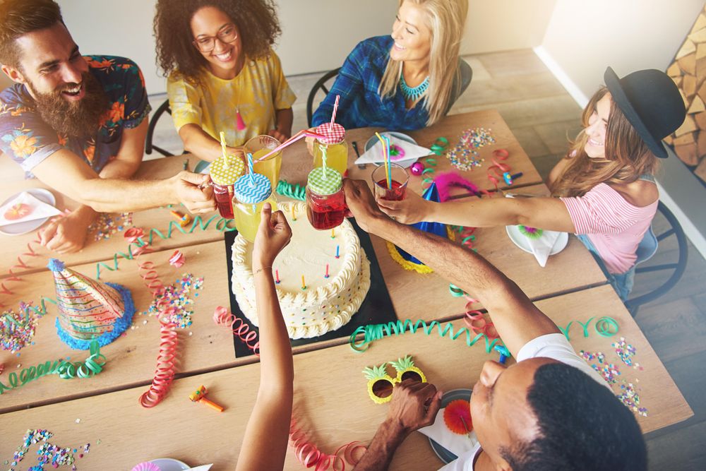 Top view of friends toasting cocktails over a cake