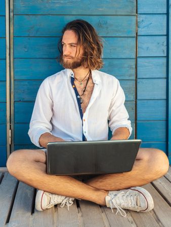 Cheerful guy using laptop near blue wall