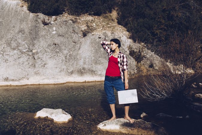 woman standing on rock with case near clear water in lake