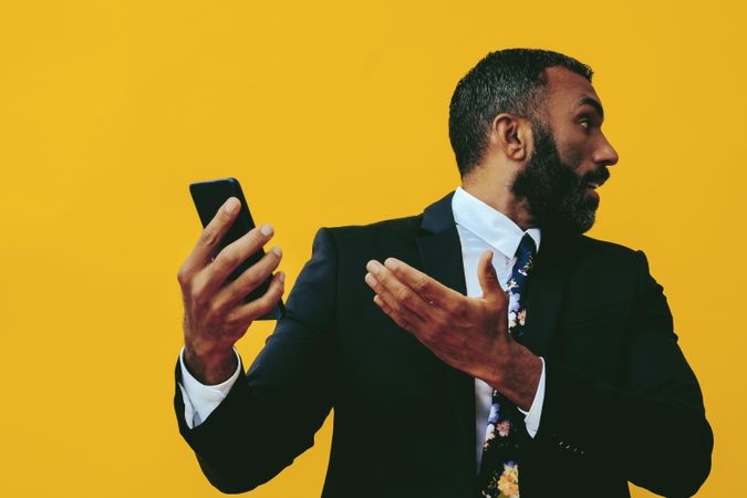 Serious Black businessman in suit gesturing at smartphone screen while looking away