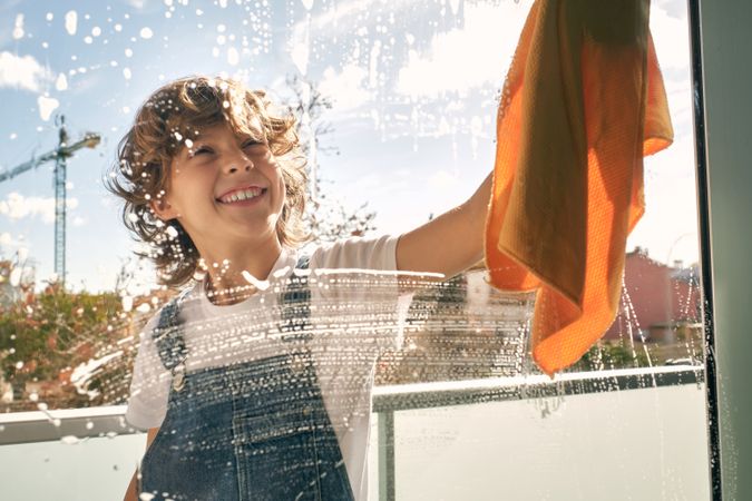 Happy kid cleaning window and smiling
