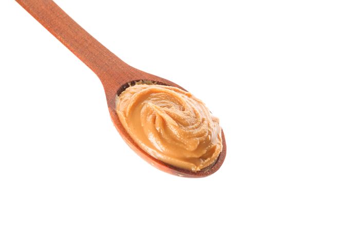 Creamy peanut butter in wooden spoon isolated on light background, closeup. A traditional product of American cuisine