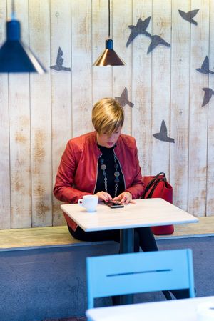 Woman in red coat texting on cell phone in wooden lined cafe