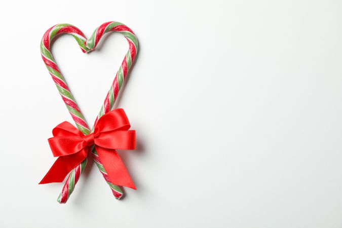 Sweet candy canes with bow on blank background, space for text