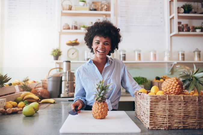 Portrait of cheerful young woman standing behind juice bar with a pineapple