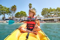 Cheerful kid paddling boat in ocean near beach