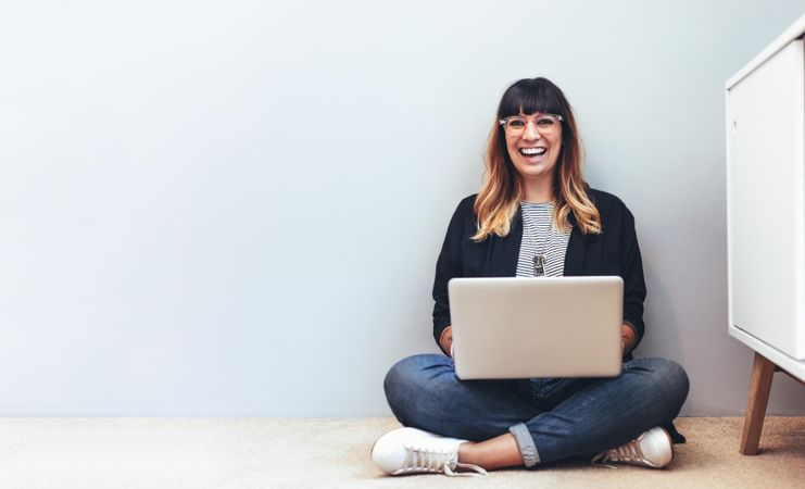 Woman entrepreneur working on laptop sitting at home smiling and looking at camera
