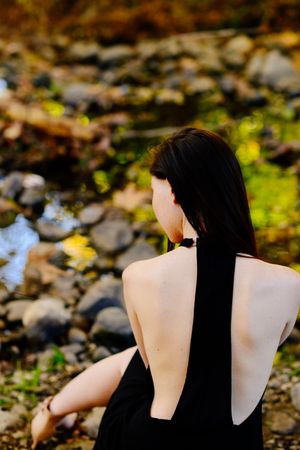 Back view of woman in dress sitting by a creek in nature
