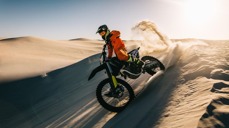 Motocross bike rider accelerating over sand dune