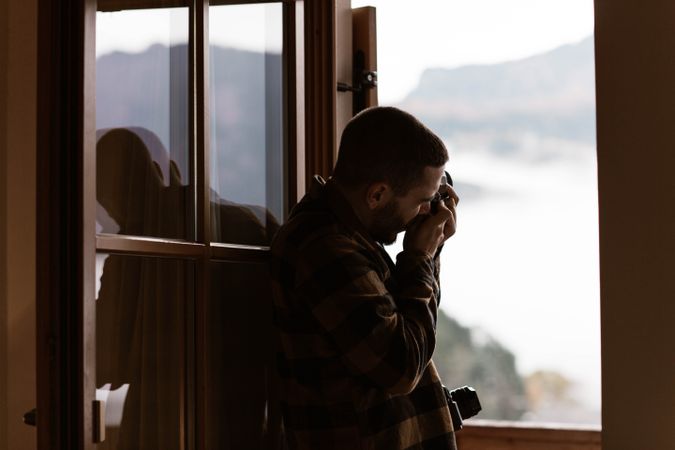 Male photograph in casual wear taking photo from opened window