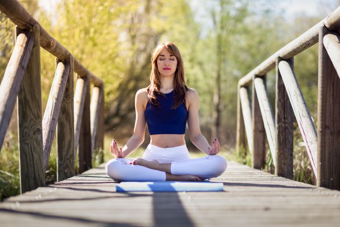 Female wearing sport clothes meditating with eyes closed on yoga mat on forest path