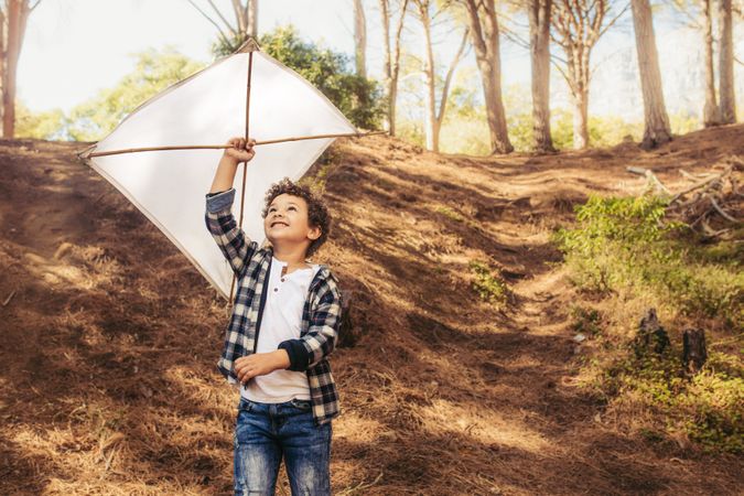 Child playing with a handmade kite in forest