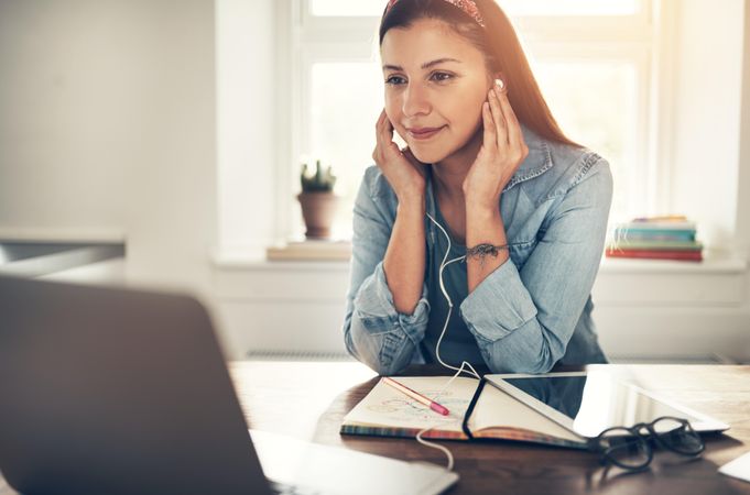 Content woman in home office listening to music on earbuds