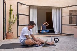 Man using laptop while woman doing yoga on terrace