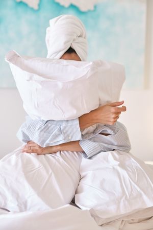 Woman hugging white pillows on bed