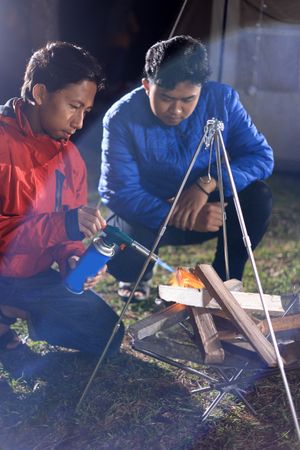 Two Young Asian Male Lighting a Campfire at a Camping Site