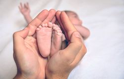Father hands holding feet of newborn lying over bed