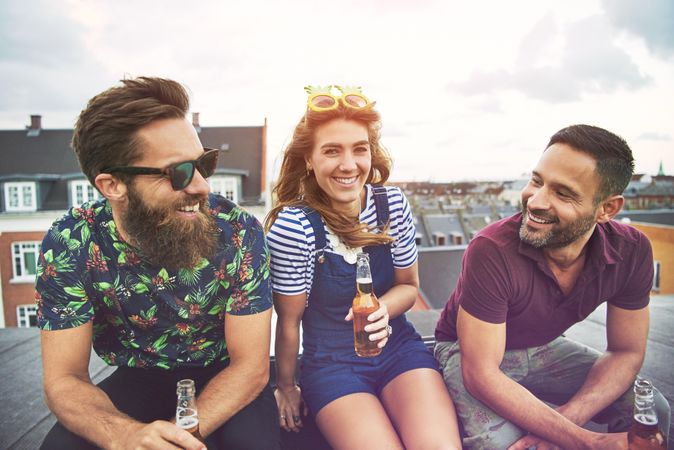 Three smiling friends relaxing with beer on the roof