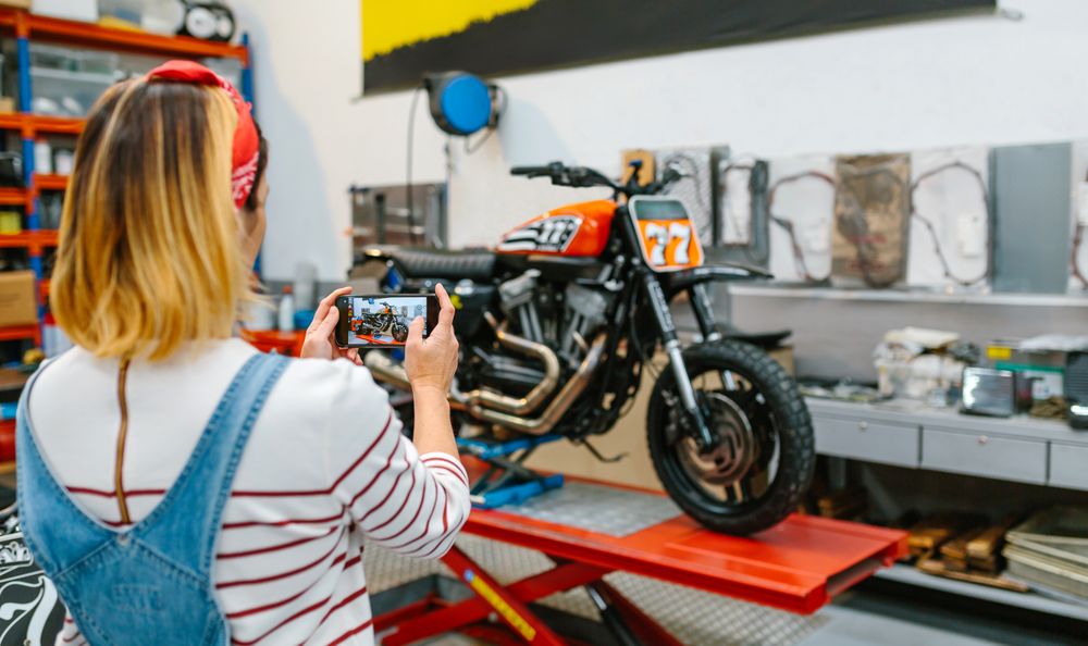 Female mechanic taking photo to motorcycle repaired over platform on garage