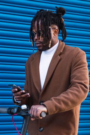 Stylish Black man with electric scooter using smartphone