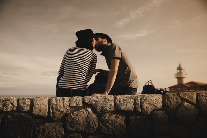 Man kissing woman on stones near lighthouse
