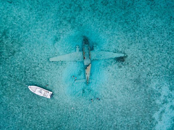 Aerial view of light boat on sea above plane sunk in water