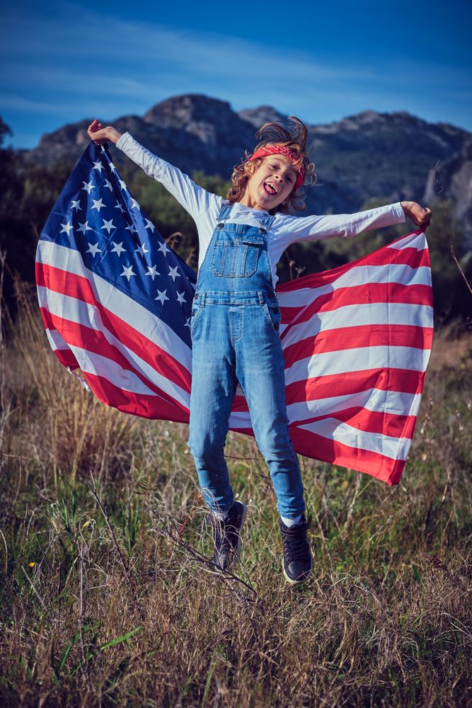 Happy preteen boy having fun with American flag in field