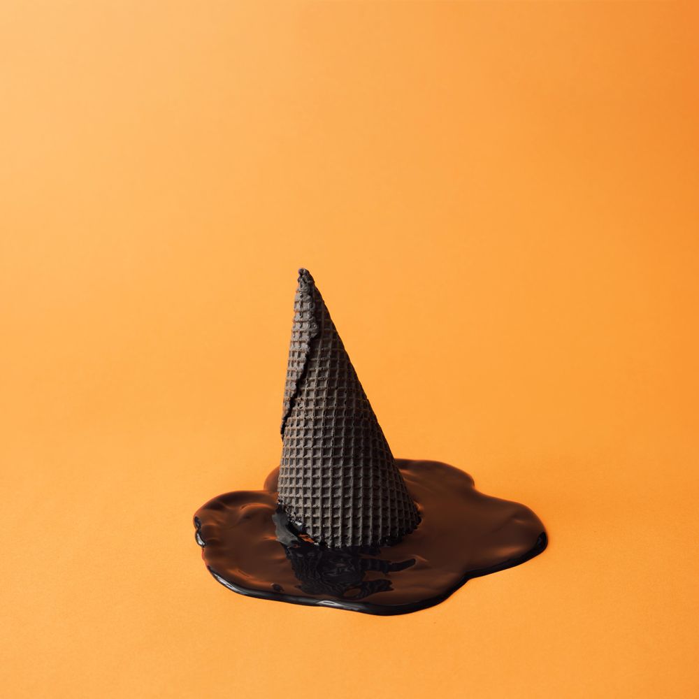 Witch hat made of ice cream cone with melted ice cream on orange background
