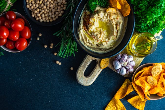 Top view of traditional hummus dip in bowl on board served with olive oil, veggies and chick peas