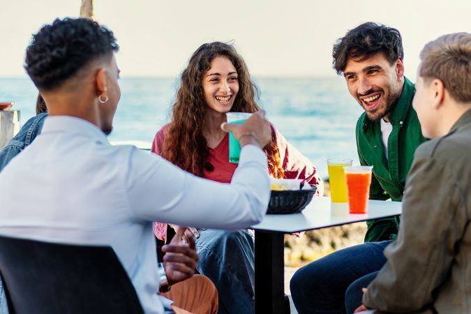 Diverse friends enjoying drinks at seaside cafe terrace with ocean view