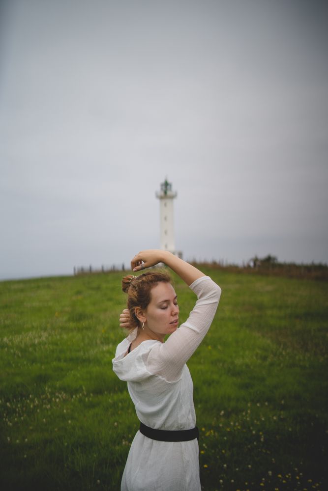 Woman walking in green meadow near lighthouse