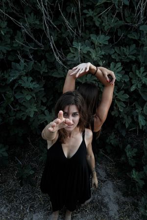 Young women posing near green bush