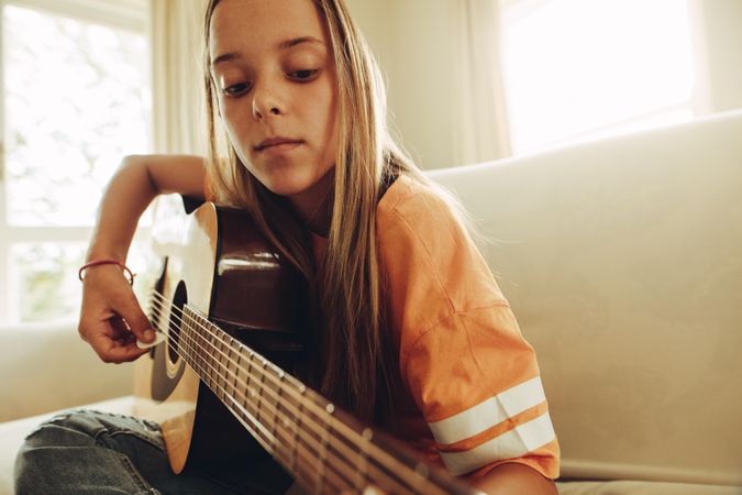 Close up of a teenage girl playing guitar sitting at home
