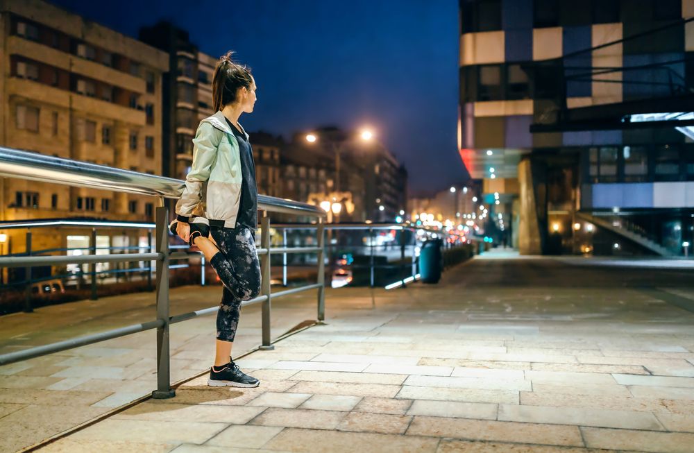 Woman runner stretching her legs in front of banister before training at night in town