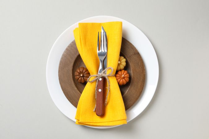 Cutlery with yellow napkin on wooden and plate on light background, top view