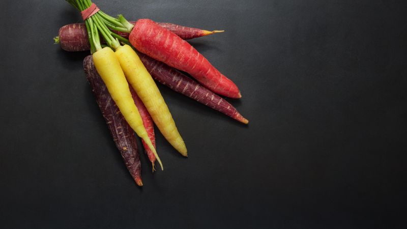 Colorful carrots bunched together on table with dark background