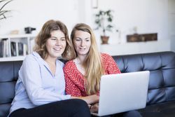 Two young women using computer while sitting on couch
