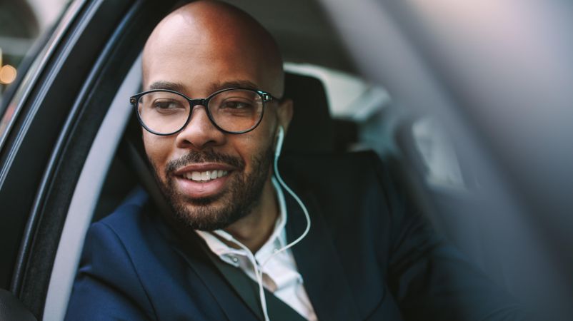 Close up of happy young businessman with earphones looking out of car window while driving