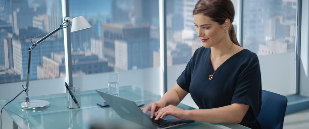 Portrait of Young Successful Businesswoman Sitting at Desk Working on Laptop Computer in City Office.