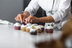Crop woman decorating cupcakes on table in kitchen