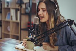 Woman recording podcast with microphone, headphones, and coffee at desk workspace