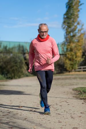 Grey haired man in red shirt and glasses jogging outside looking down