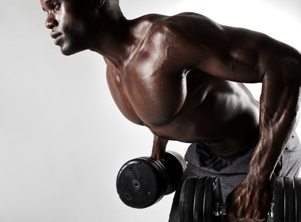 Shirtless young man working out with heavy dumbbells on grey background