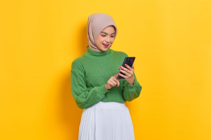 Calm woman in headscarf looking down and using her smart phone