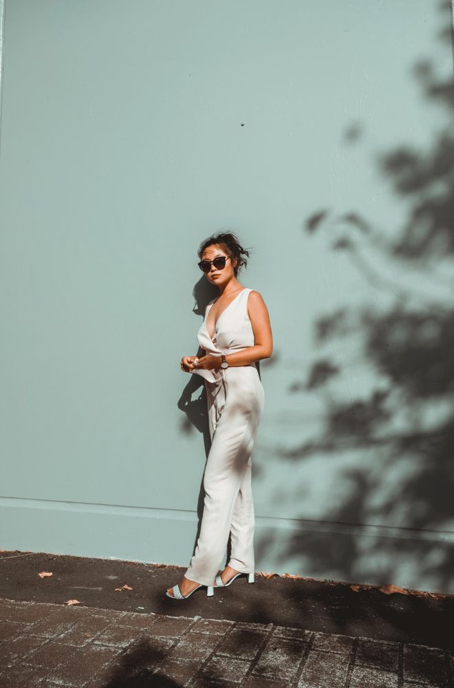 Woman in light jumpsuit in the sun in front of blue wall